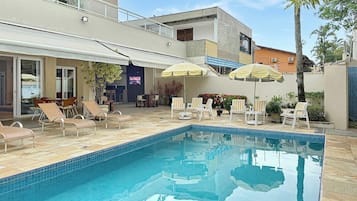 A swimming pool with lounge chairs and umbrellas, surrounded by buildings.