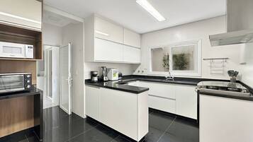 A modern kitchen with white cabinetry, a built-in microwave, a coffee maker, and a stove.
