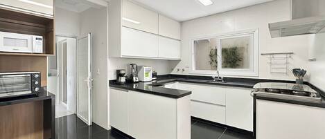 Una cocina moderna con armarios blancos, un microondas integrado, una cafetera y una estufa.