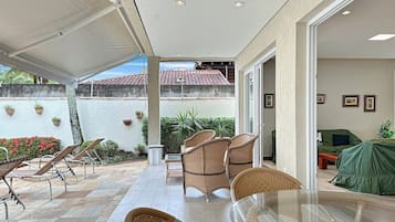 An outdoor patio area with wicker furniture, a glass table, and a view of a building with a tiled roof.