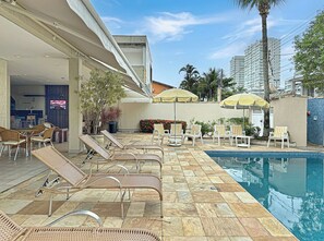 Un área junto a la piscina con sillones de descanso, piscina y sombrillas.