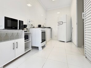 A modern kitchen with white cabinetry, a microwave, a coffee maker, and a refrigerator. - Quarto 12 (Guarujá)