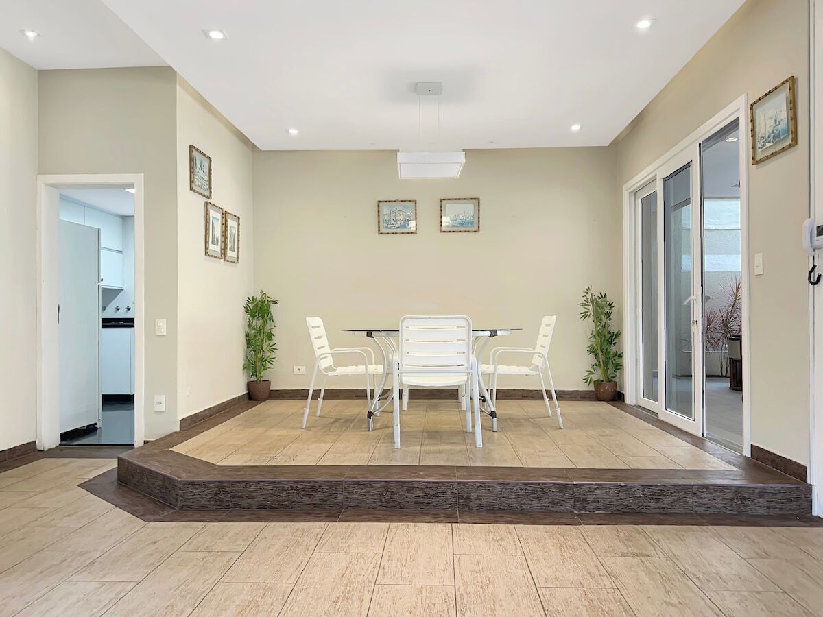 A spacious room with a dining table and chairs, a staircase, and a door leading to a balcony.