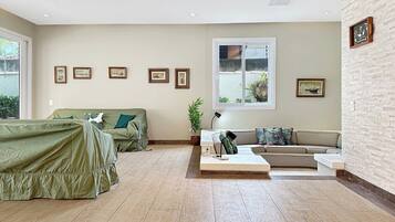 A spacious living room with a large window, a sofa set, a coffee table, and a wall-mounted picture frame.