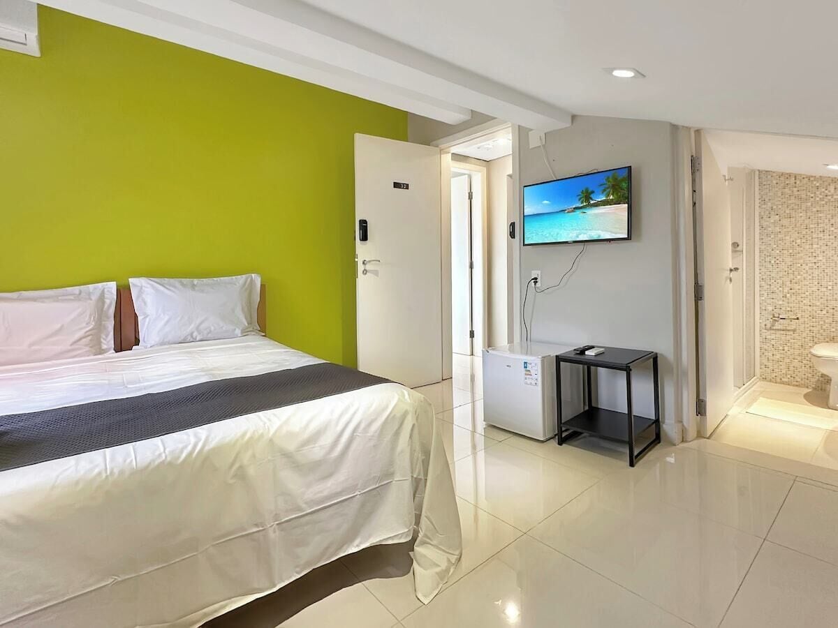 Habitación de hotel con cama, televisor, una mesita y un baño a la vista a través de una puerta abierta.
