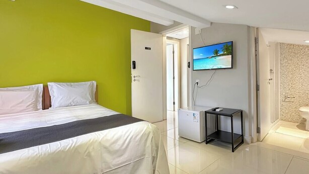 Una camera d'albergo con un letto, una televisione, un tavolino e un bagno visibile attraverso una porta aperta.