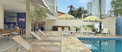 A poolside area with lounge chairs, a pool, and umbrellas.