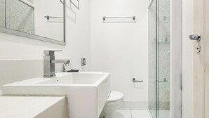 Casa de banho moderna com lavatório branco, sanita e cabine de duche em vidro.