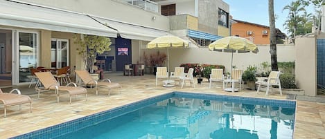 Una piscina con lettini e ombrelloni, circondata da edifici.