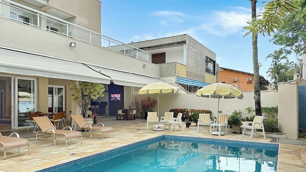 Piscina com espreguiçadeiras e guarda-sóis, cercada por edifícios.