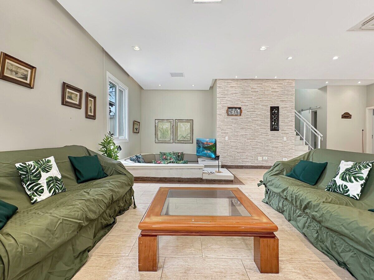 A modern living room with two green sofas, a glass coffee table, and a brick accent wall.