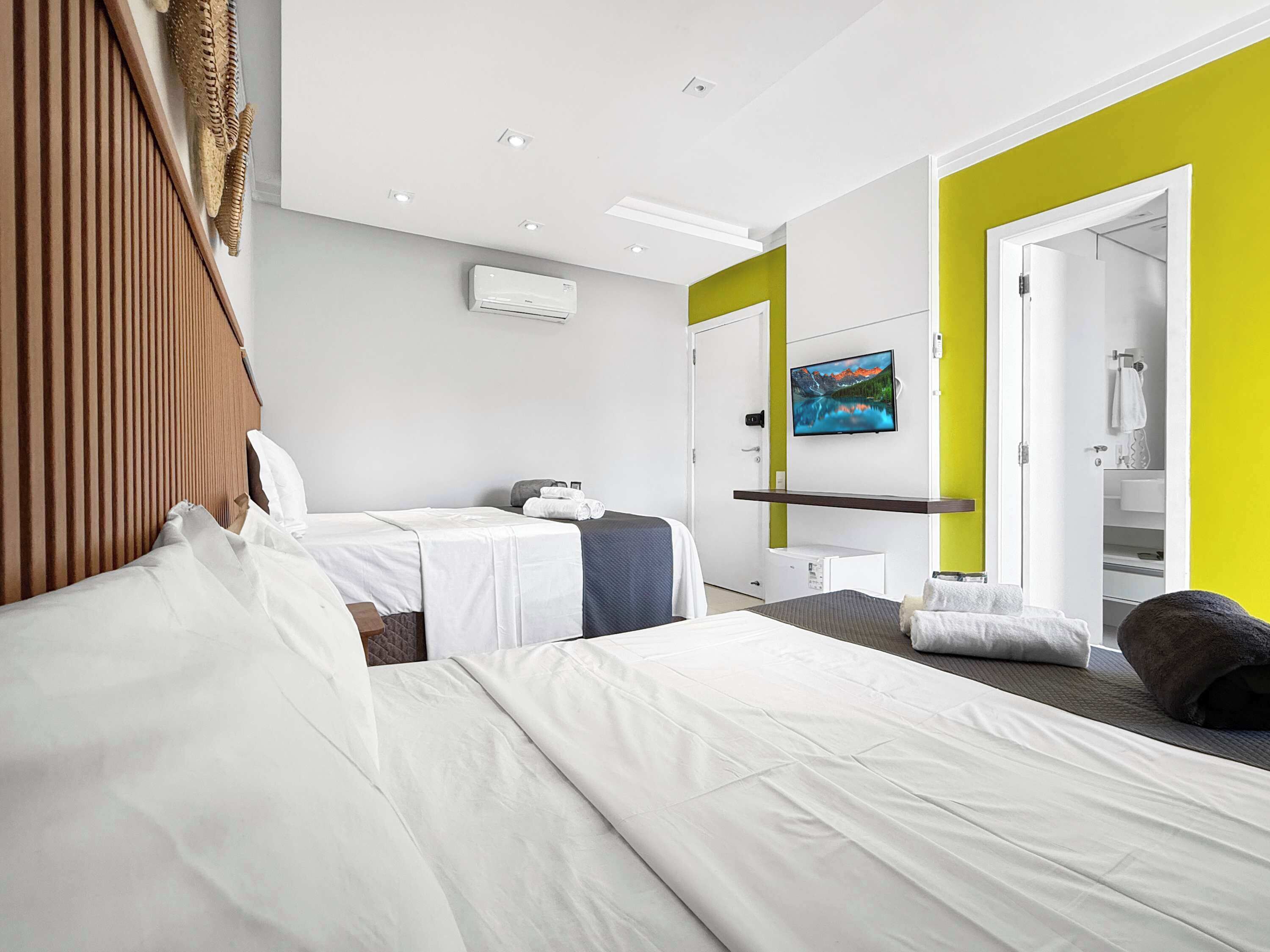 A hotel room with two beds, a television, an air conditioning unit, and a bathroom visible through an open door.
