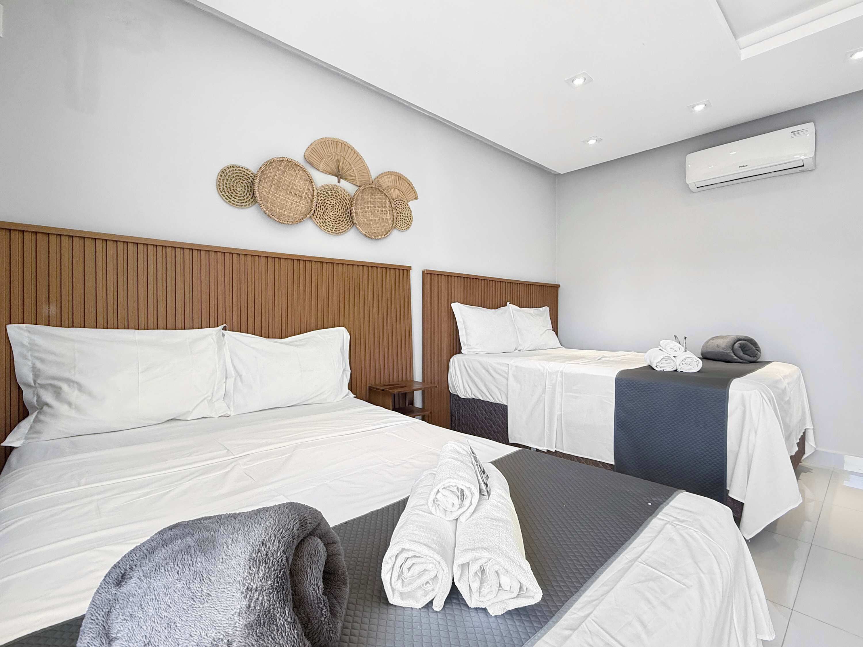 Habitación de hotel con dos camas, cabecera de madera, aire acondicionado de pared y un adorno en la pared.