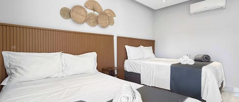 Ett hotellrum med två sängar, en sänggavel i trä, en väggmonterad luftkonditioneringsanläggning och en dekorativ väggdekoration.