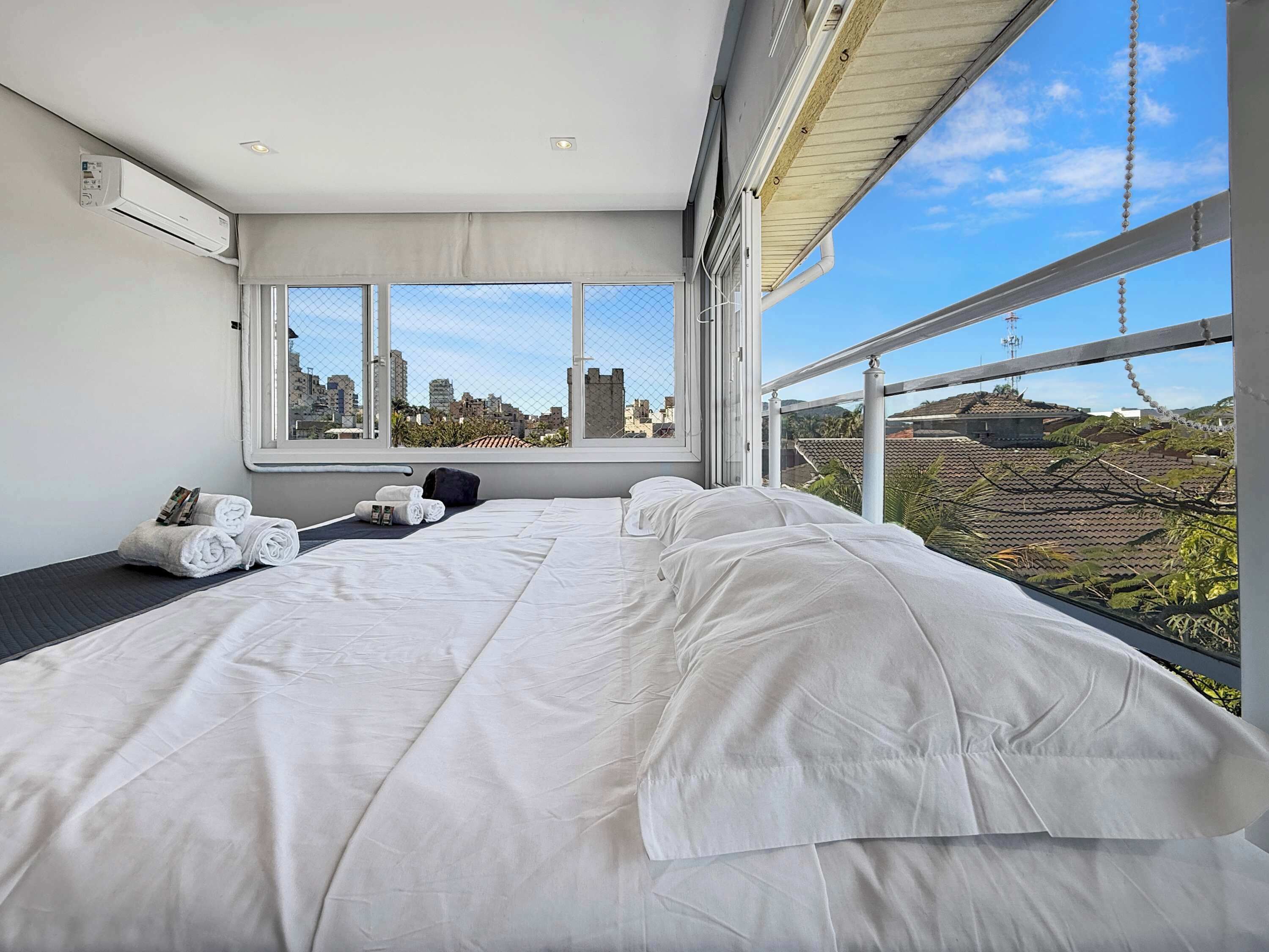 Quarto de hotel moderno com uma cama grande, janela com vista para a cidade e aparelho de ar condicionado.