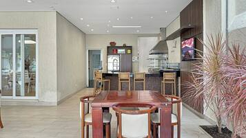 A modern dining area with a wooden table and chairs, a kitchen in the background, and a potted plant on the right.