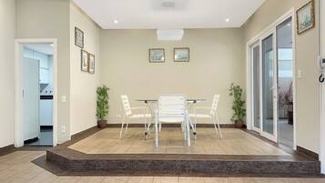 A spacious room with a dining table and chairs, a large window, and a door leading to another room.