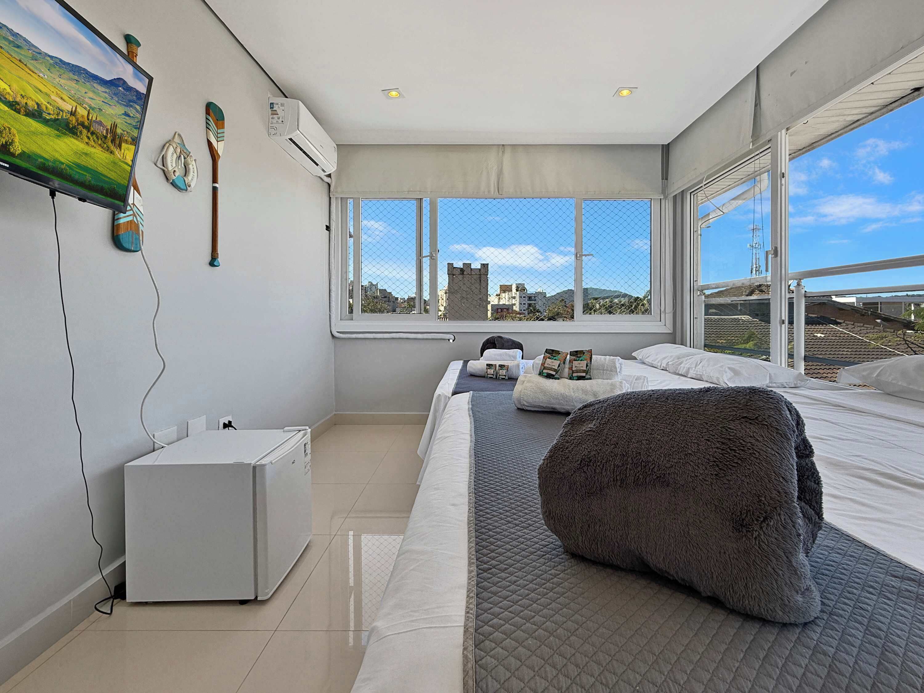 Une chambre moderne avec un grand lit, un téléviseur à écran plat, une petite armoire blanche et une fenêtre donnant sur la ville.