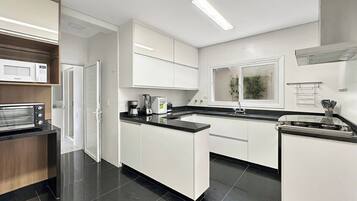 A modern kitchen with white cabinetry, a built-in microwave, a stove, and a coffee maker.