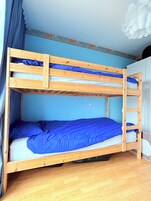 Uma cama beliche com escada, colchão azul e piso de madeira.