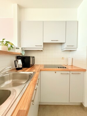 Eine Küche mit weißen Schränken, einer Holz Arbeitsplatte, einer Edelstahlspüle, einer Kaffeemaschine und einer Mikrowelle.