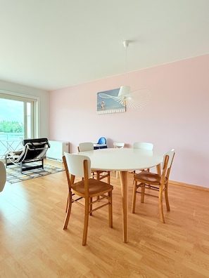 Un comedor con una mesa blanca y sillas de madera, una lámpara colgante y un cuadro en la pared.