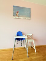 Quarto com piso de madeira, uma cadeira branca, uma cadeira alta azul e um quadro de uma cena de praia na parede.