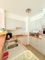 Una cocina moderna con armarios blancos, encimera de madera, un fregadero con escurreplatos y diversos electrodomésticos.