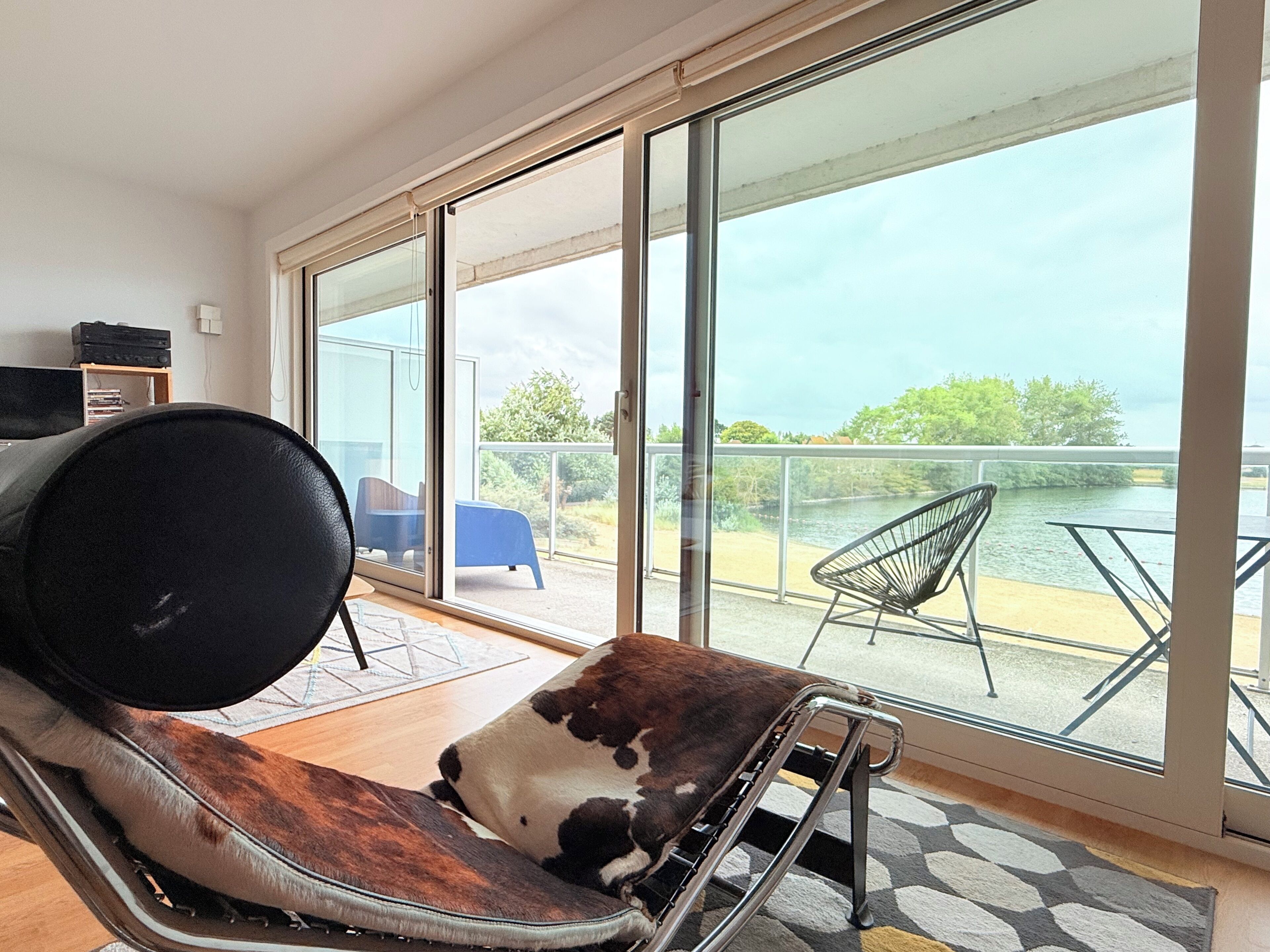 A modern room with a large sliding glass door leading to a balcony with a view of a body of water.