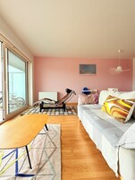 Uma sala de estar moderna com sofá, mesa e cadeira. Há uma janela com vista para bicicletas do lado de fora.