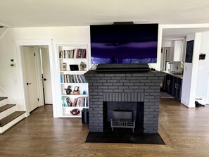 A living room with a fireplace, a bookshelf, and a kitchen area.