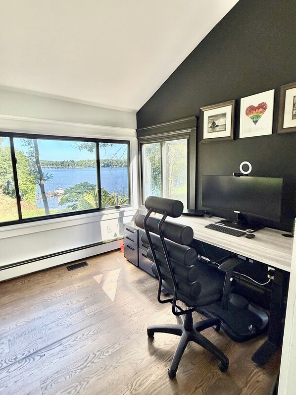 A modern office with a large window overlooking a body of water, a desk with a computer, and a chair.