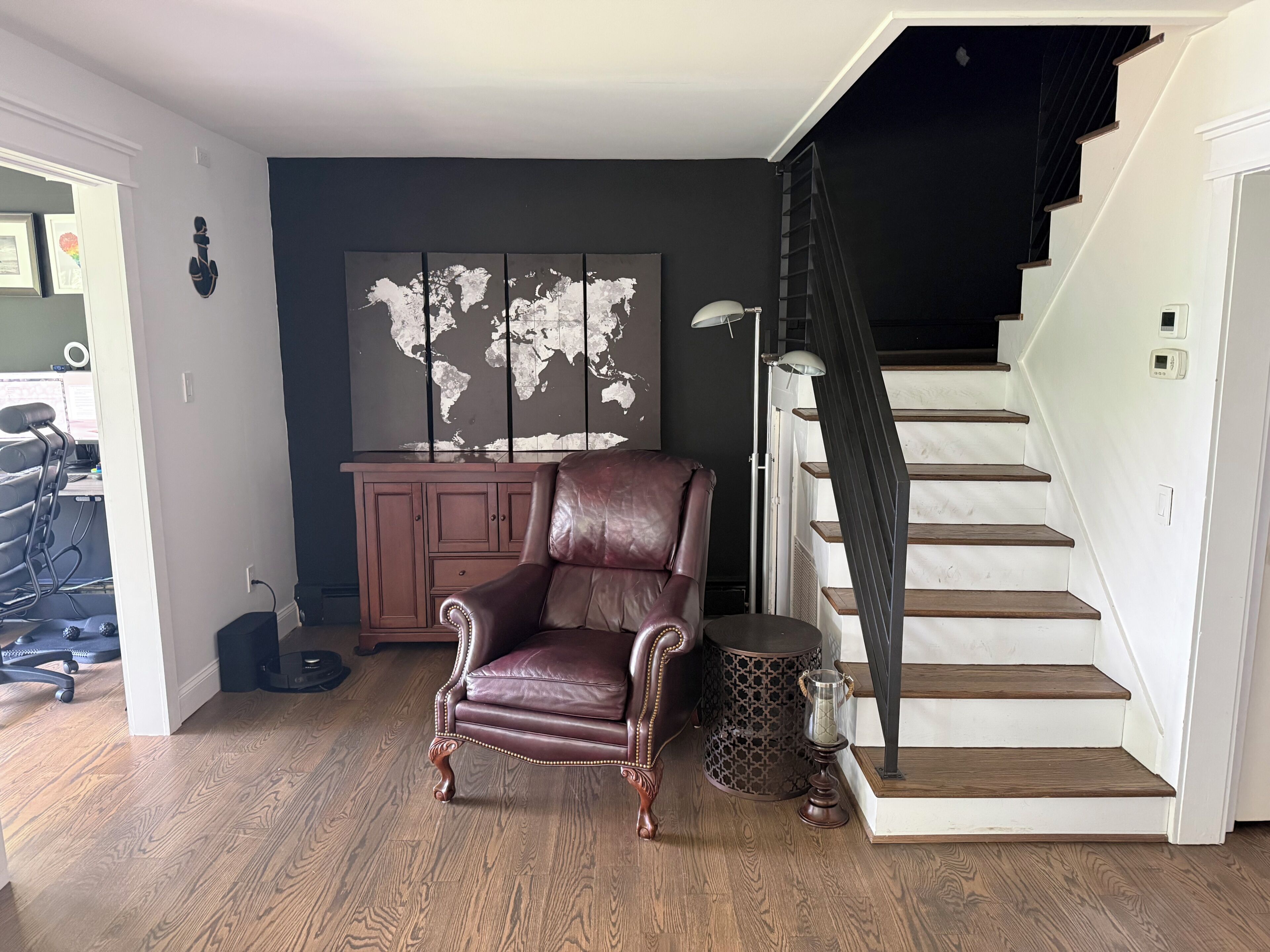 Une pièce avec un fauteuil en cuir marron, une carte du monde accrochée au mur, un escalier et un meuble.