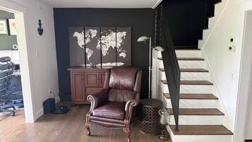 Une pièce avec un fauteuil en cuir marron, une carte du monde accrochée au mur, un escalier et un meuble.