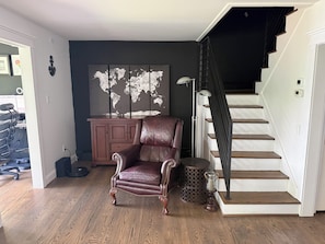 A room with a brown leather chair, a world map on the wall, a staircase, and a cabinet.