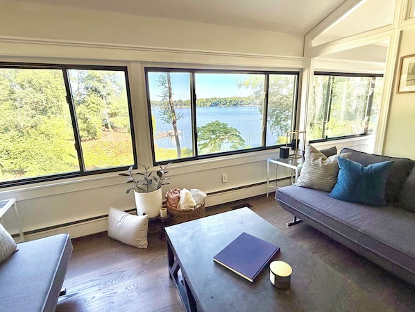A living room with a view of a lake, a sofa, a coffee table, and a bookshelf.