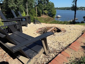 A lakeside patio with Adirondack chairs, a fire pit, and a view of the lake.