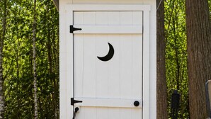 Un cobertizo de madera blanca con un símbolo de luna creciente en la puerta, un picaporte metálico y una pequeña ventana.