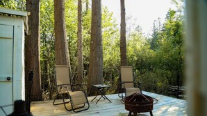 Una terraza de madera con dos sillas y una mesa pequeña, rodeada de árboles altos.