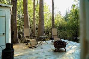A wooden deck with two chairs and a small table, surrounded by tall trees.