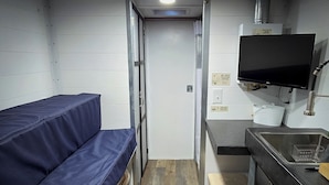 Una kitchenette compacta con un lavamanos, estufa y televisor de pantalla plana montado arriba.