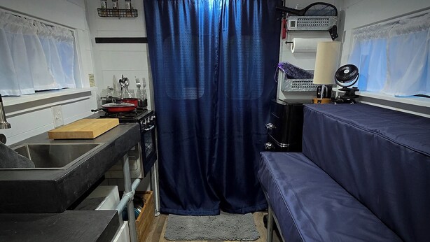 Cocina pequeña con pileta, estufa y una cortina azul.