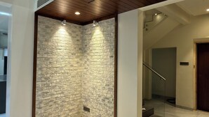 A spacious interior with a high ceiling, a stone wall, and a staircase leading to an upper level. - 3BHK Pavillion Penthouse Near Viman Nagar by Velvet Stays (Pune)