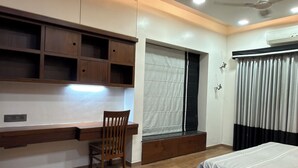 A bedroom with a bed, wooden floor, built-in desk, chair, and ceiling fan. - 3BHK Pavillion Penthouse Near Viman Nagar by Velvet Stays (Pune)