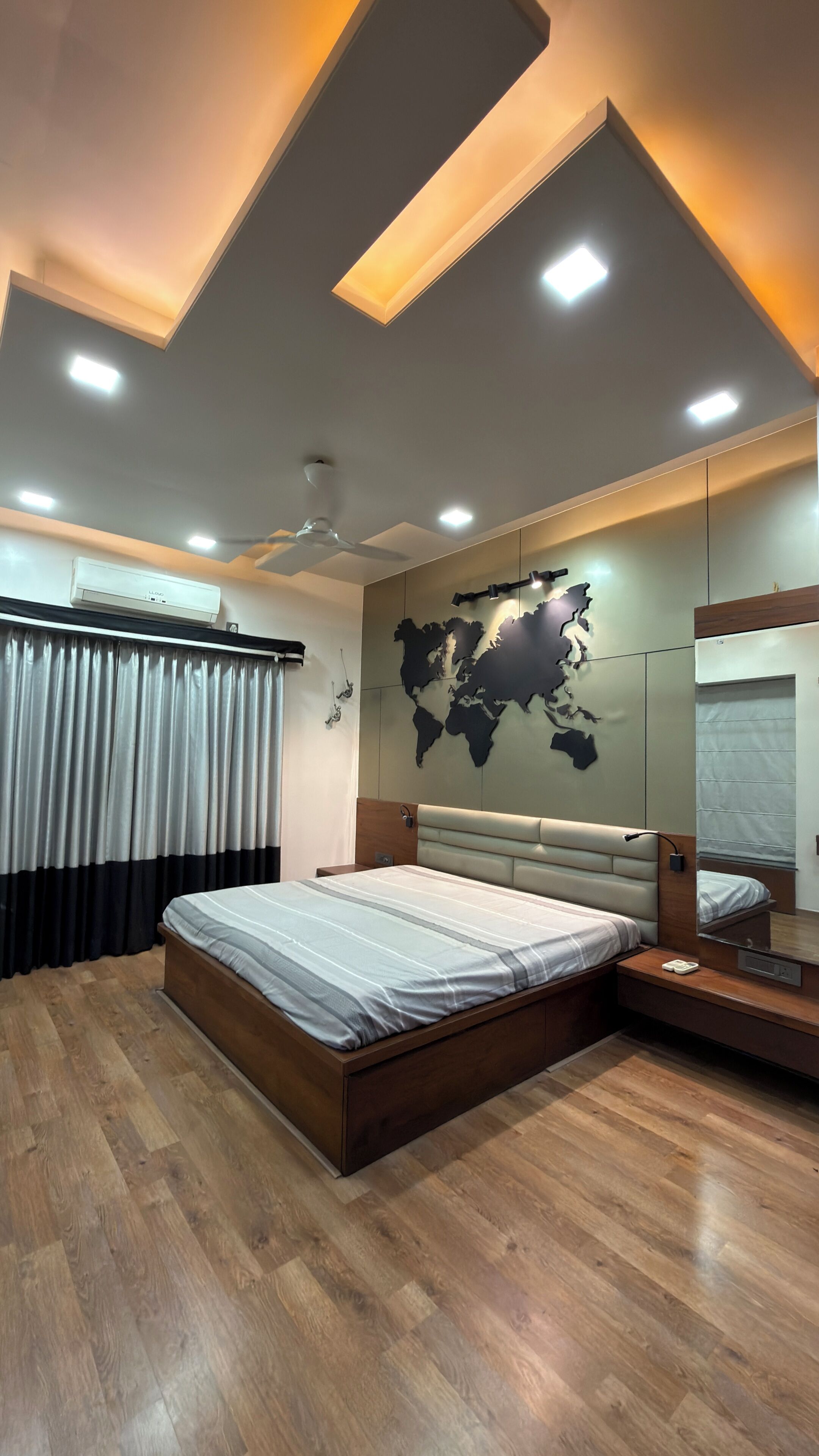 A bedroom with a large bed, a ceiling fan, recessed lighting, a world map on the wall, and a mirror.