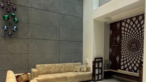 A modern living room with a sectional sofa, a decorative wall with geometric shapes, and a patterned wall divider. - 3BHK Pavillion Penthouse Near Viman Nagar by Velvet Stays (Pune)