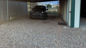 A gravel driveway leading to a covered parking area with a vehicle parked inside.