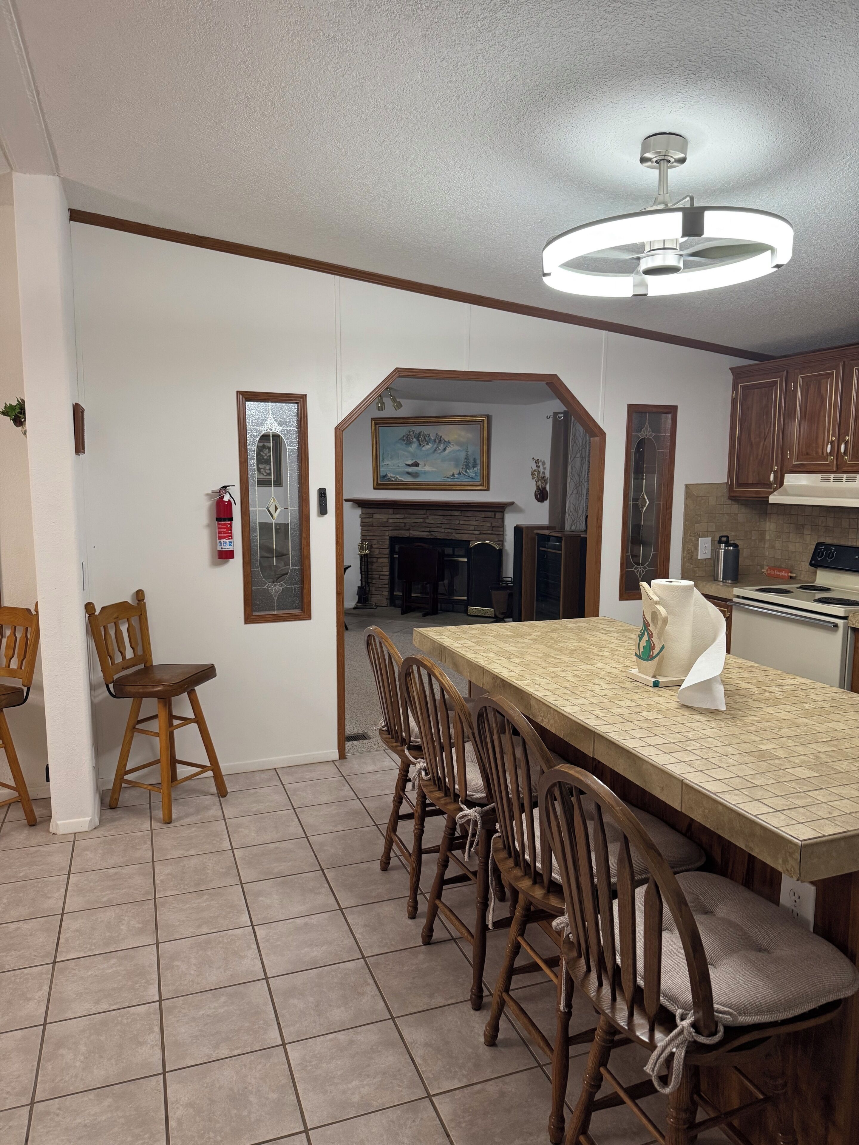 A dining area with a long table, wooden chairs, a ceiling fan, and a fireplace.