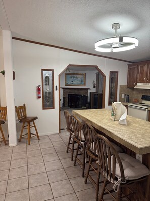 A dining area with a long table, wooden chairs, a ceiling fan, and a fireplace.