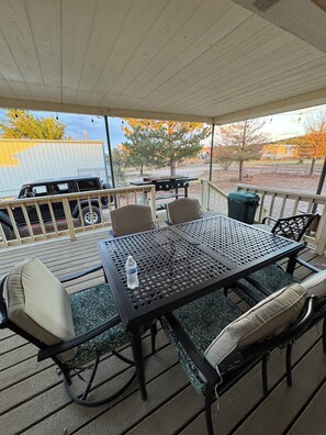 An outdoor patio with a table and chairs, a grill, and a vehicle in the background.